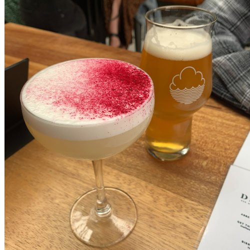 A cocktail with pink dust on top and a beer on a table